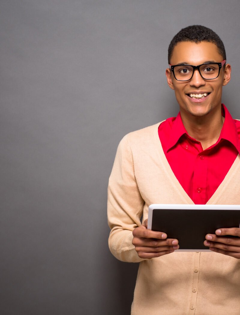 Handsome latin student holsing tablet PC in studio. Toothy smiling man inglasses going to classes to University.